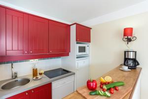 a kitchen with red cabinets and fruits and vegetables on a counter at Résidence Pierre & Vacances Le Domaine de Gascogne in Biscarrosse