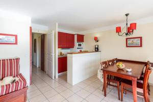 cocina y comedor con armarios rojos y mesa en Résidence Pierre & Vacances Le Domaine de Gascogne, en Biscarrosse