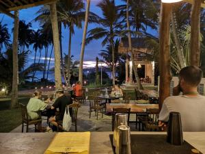 people sitting at tables at a restaurant with palm trees at Singhe House in Dickwella