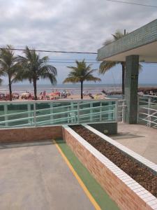 a beach with palm trees and a building with a fence at Apartamento Temporada pé na areia in Mongaguá