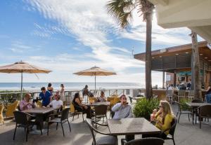 a group of people sitting at tables on a patio with the beach at Tides Folly Beach in Folly Beach