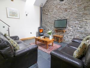 a living room with leather furniture and a stone wall at Yr Hen Beudy in Aberystwyth