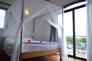 a bedroom with a canopy bed and a balcony at Villa Malandy Appart Hôtel Duplex 2 in Nosy Be