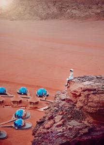 a person sitting on top of a cliff in the desert at Memories Aicha Luxury Camp in Wadi Rum