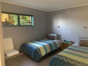 a bedroom with two beds and a chair and a window at Beach Lane Apartment in Whangarei
