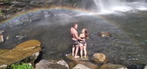 a man and woman standing in front of a waterfall with a rainbow at Dong Loan Hotel in Bản Na Bâ
