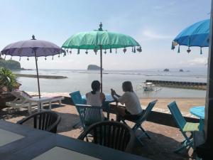 two women sitting in chairs under umbrellas on the beach at Puri Oka Beach Bungalows in Candidasa