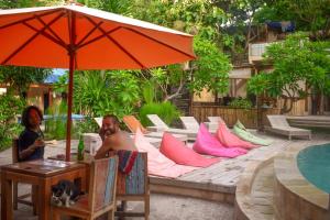 two men sitting under an umbrella next to a pool at Jati Village, Party Hostel and Bungalows in Gili Trawangan