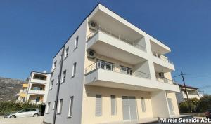 a white building with a car parked in front of it at Apartment Seaside Mireja in Kaštela