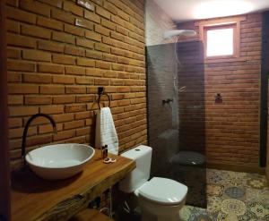 uma casa de banho com um lavatório, um WC e uma parede de tijolos. em Pousada Café da Mata em Alto Caparaó