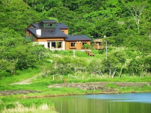 ein Holzhaus auf einem Hügel neben einem See in der Unterkunft ポロト案内舎 in Hamanaka