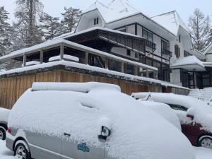 ein Haus mit schneebedeckten Autos davor geparkt in der Unterkunft Powder Temple in Hakuba