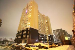 a tall building with cars parked in a parking lot at Апартаменты на пр Победы OrenRoom in Orenburg