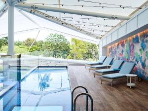 uma piscina interior com cadeiras e um quadro na parede em Crystalbrook Flynn em Cairns