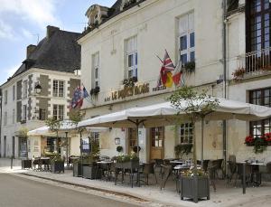 un restaurant avec des tables et des parasols en face d'un bâtiment dans l'établissement Logis Hôtel Restaurant Le Puits Doré, à Richelieu