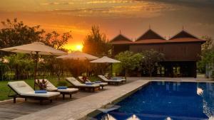 een zwembad met ligstoelen en parasols bij zonsondergang bij Mane Hariharalaya in Siem Reap