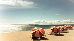 una línea de sillas de playa con sombrillas en una playa en LAppart Empuriabrava, en Empuriabrava