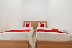 two beds in a room with white walls and red pillows at RedDoorz @ Graha Cemerlang Maros in Makassar