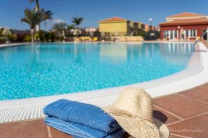 um chapéu e toalha sentados num banco ao lado de uma piscina em Duplex luxury Meloneras Hill em Maspalomas
