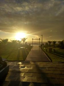 a sunset on a beach with palm trees and a boardwalk at Rota do Sol Praia Hotel in Guaratuba