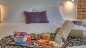 een dienblad met ontbijtproducten op een bed bij Rosebourne Gardens Motel in Woolgoolga