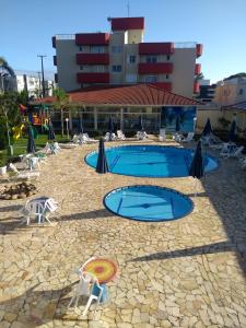 Hotel Rota do Sol في غواراتوبا: مسبح فيه مظلات وكراسي امام مبنى