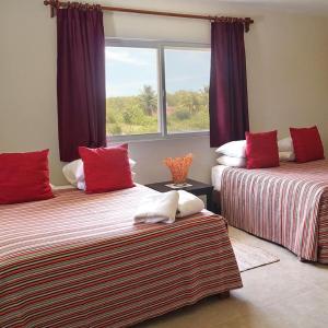 a room with two beds with red pillows and a window at Los Depas del Aeropuerto Holbox in Holbox Island