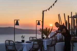 a man holding a plate at a table with a sunset in the background at Cocoon Suites in Imerovigli