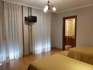 1 dormitorio con 2 camas y TV en la pared en Hostal Virgen del Villar, en Laguna de Duero