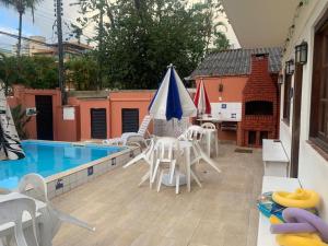 uma piscina com cadeiras brancas e um guarda-sol azul em Hotel Canto da Enseada no Guarujá