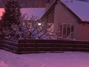 a house with a tree and a fence in the snow at Linmore in Aviemore