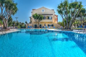 a swimming pool in front of a house with palm trees at Legends Hotel Sidari Corfu in Sidari