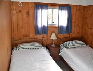 two beds in a room with wooden walls and a window at Barney’s Lakeside Resort in Puntzi Lake