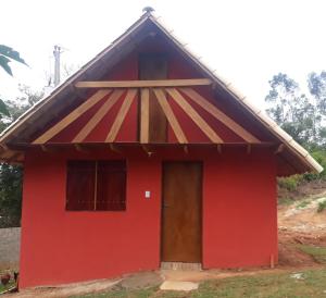 una casa rossa con tetto di paglia di SITIO CAMINHO DAS PEDRAS - Suítes e Chalés a São Thomé das Letras