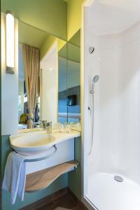 een badkamer met een wastafel, een bad en een spiegel bij ibis budget Flensburg Handewitt in Handewitt