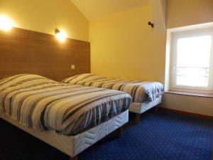 two beds in a hotel room with a window at Logis Hôtel Restaurant Les Cévennes in Saint-Cirgues-en-Montagne