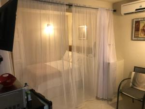 ein Schlafzimmer mit weißen Vorhängen, einem Stuhl und einem TV in der Unterkunft Glynver Apartments in Christchurch