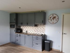 a kitchen with gray cabinets and a clock on the wall at Vakantiewoning Koegras in Julianadorp