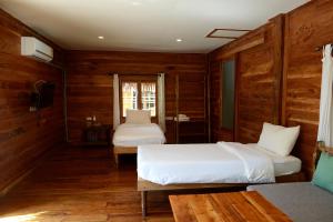 two beds in a room with wooden walls at Baan​ Tonlamphu​ Pakpra in Phatthalung