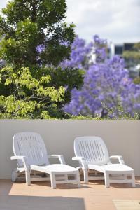 dos sillas blancas sentadas junto a una pared con flores en The Oasis Apartments, en Brisbane