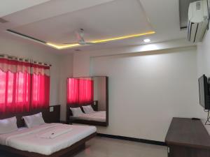 a bedroom with two beds with red curtains and a mirror at Hotel Adarsh in Aurangabad