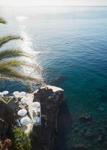 a beach with a palm tree and the ocean at Reid's Palace, A Belmond Hotel, Madeira in Funchal