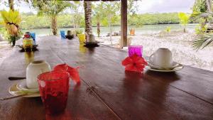 a wooden table with plates and cups and a glass at Casinha Amarela EcoLodge Boipeba in Ilha de Boipeba