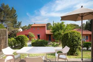 a table and chairs and an umbrella in front of a red house at SOWELL RESIDENCES Chênes Verts in Saint-Raphaël