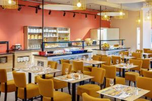 a restaurant with tables and yellow chairs and a kitchen at SOWELL RESIDENCES Chênes Verts in Saint-Raphaël