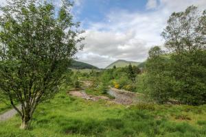 a river in the middle of a field with trees at Glamping Hut - By The Way Campsite in Tyndrum
