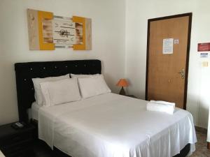 a bedroom with a bed with white sheets and a door at Pousada Pollyana in Pirenópolis