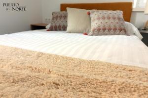 uma cama com um cobertor branco e almofadas em Apartamentos Puerto Norte - Apto 2 em Veiga