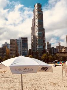 un ombrellone bianco su una spiaggia con un edificio alto di Unlimited - Frente ao Mar. Apt todo mobiliado. a Santos