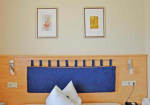 a bed with a blue headboard and two pictures on the wall at Hotel Haus Schons in Mettlach